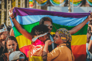 Gente en marcha. Una persona sostiene una bandera de arcoirirs LGBT y un adulto abraza a un nino 